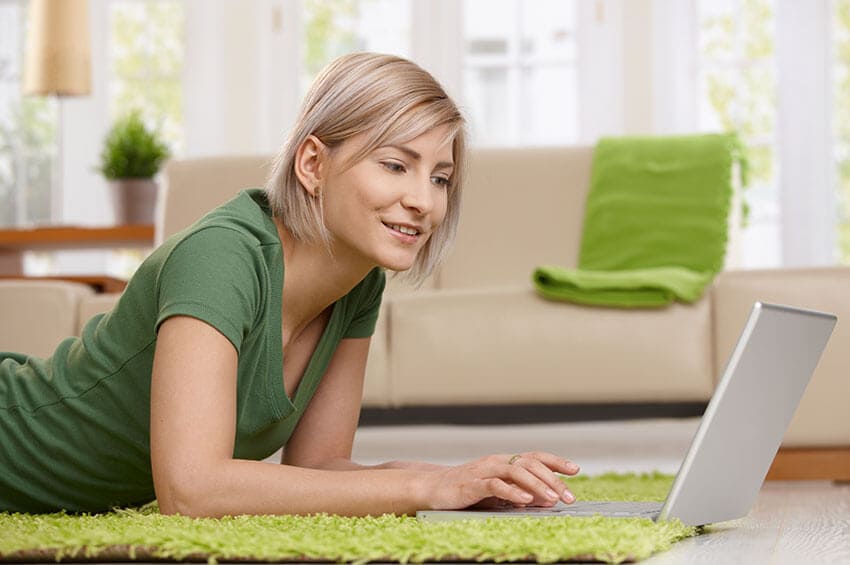 The image depicts a professionally operated van from Hire Man and Van positioned on a residential street in Strand, with the vehicle's side door closed. The van features a clean exterior with a white finish and subtle branding, partially visible in the frame. In the foreground, there is a neatly stacked collection of waste materials comprising black plastic rubbish bags, flattened cardboard boxes, and small loose items such as an empty plastic container and a discarded cushion, indicating a typical household clearance. The waste is arranged on the paved pavement, close to the curb, with some items leaning against the side of the van. The surrounding environment includes a brick-built residential terrace with front gardens, some greenery visible in the background, and parked cars along the street. The sky appears overcast, casting diffuse daylight over the scene, which is characteristic of a typical day for a rubbish removal service. This imagery reflects a standard household waste collection scenario, aligning with the services offered by Hire Man and Van in the WC2 area.